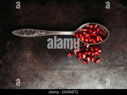 Semi di melograno in cucchiaio su sfondo rustico scuro. Messa a fuoco selettiva. Profondità di campo poco profonda. Foto Stock