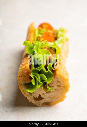 Gustosi hot dog freschi con salsiccia alla griglia, senape francese e foglie di insalata fresca sullo sfondo rustico. Messa a fuoco selettiva. Profondità di campo poco profonda. Foto Stock