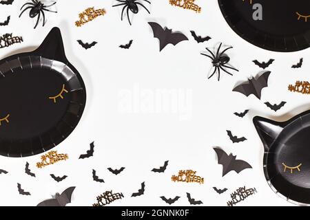 Nero gatto a forma di carta Halloween party piatti, pipistrelli e felice Halloween testo confetti su sfondo bianco Foto Stock
