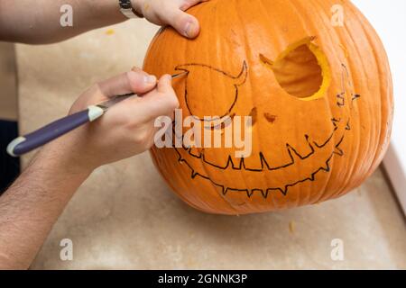 Mani umane che fanno faccia della zucca di Halloween con coltello per decorare la festa di Halloween. Processo di produzione di jack-o-lanterna a casa. Foto Stock