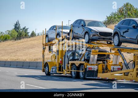 Commerciale giallo brillante Big RIG trasportatore industriale di auto semi-camion trasporto di auto sul lungo semirimorchio idraulico modulare a due livelli che gira sulla a. Foto Stock