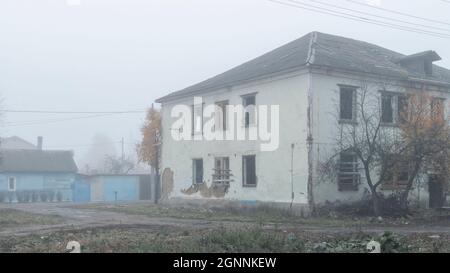 Una casa in legno abbandonata a due piani sulla strada in una giornata di nebbia Foto Stock