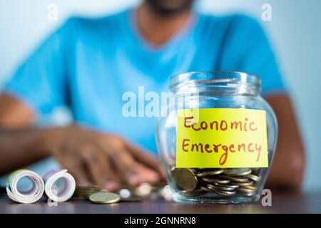 Concetto di emergenza economica - l'uomo irriconoscibile contando denaro prendendo le monete raccolte dal vaso Foto Stock