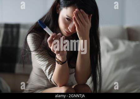 Donna sconvolto che tiene il test di gravidanza mentre si siede sul divano Foto Stock