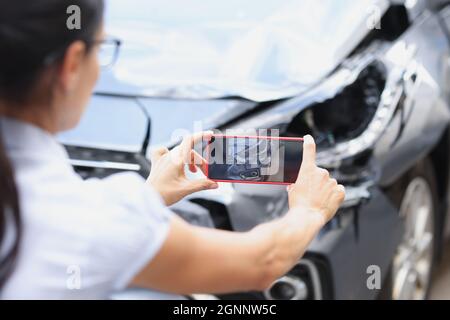 La donna dell'agente di assicurazione scatta le foto dallo smartphone dei danni dell'automobile dopo l'incidente stradale Foto Stock