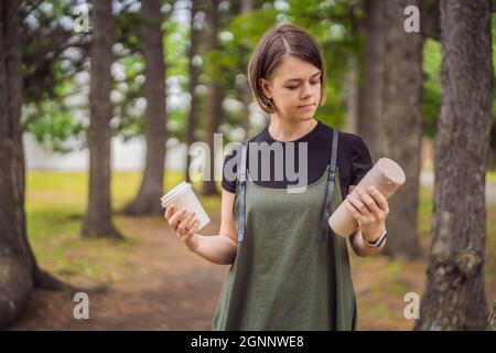 Ritratto di felice sorridente giovane donna confrontando thermo tazza o Tumbler con carta da caffè usa e getta tazza Foto Stock