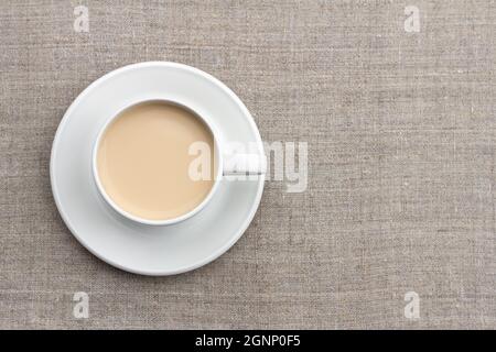 Tè piccante con latte e miele in una tazza di porcellana bianca su sfondo tessile Foto Stock
