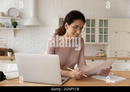 Donna caucasica sorridente lavora con documenti a casa Foto Stock