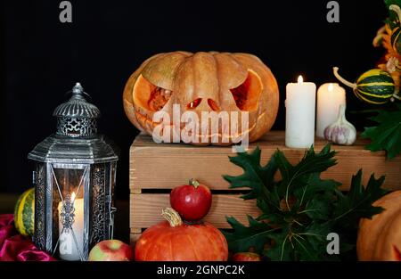 Concetto di Halloween: Zucche, candele, girasole, foglie, lanterna e altri attributi al tavolo come sfondo tema Halloween. Zucca di Halloween con faccia spaventosa. Foto di alta qualità Foto Stock