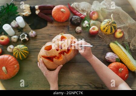 Halloween Concept: Vista dall'alto della zucca da intaglio femminile. Donna carves una bocca in una zucca per fare un jack o'lantern su un tavolo di legno con verdure. Immagine di alta qualità Foto Stock