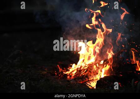 Scintille calde rosse che bruciano volano dal fuoco grande. Carboni brucianti, particelle che fiammano che volano su sfondo nero. Foto Stock
