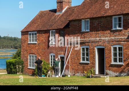 Buclers Hard, un pittoresco villaggio nella New Forest in Hampshire, Inghilterra, Regno Unito, con operai che effettuano la manutenzione sui cottage storici Foto Stock