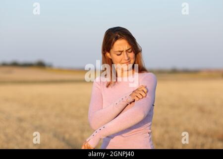 Donna stressata graffiando il braccio itchy in un campo raccolto Foto Stock