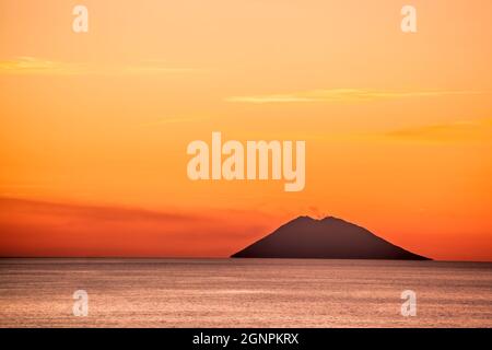 Vulcano attivo Stromboli contro il tramonto colorato in Italia, vista dalla costa calabrese. Foto Stock