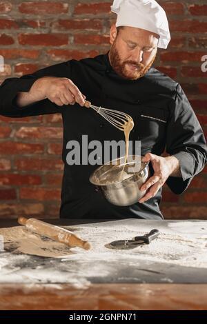 Ritratto di rosso-bearded uomo, chef, cuoco in nero uniforme cucina fa pasta di pane al caffè, cucina del ristorante. Concetto di dieta sana, nazionale Foto Stock