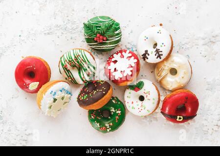 Ciambelle di Natale smaltate in casa. Ciambelle smaltate in casa assortite con spolverini su sfondo bianco festivo. Vista dall'alto, spazio vuoto Foto Stock
