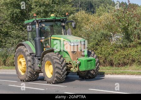 Trattore agricolo John Deere verde e familiare su una strada rurale aperta in salita. Il modello Deere con pneumatici grandi è 7310 R. Foto Stock