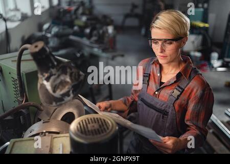 Vista ad angolo elevato di donna industriale di media età adulta che lavora in ambienti interni in officina metallica. Foto Stock