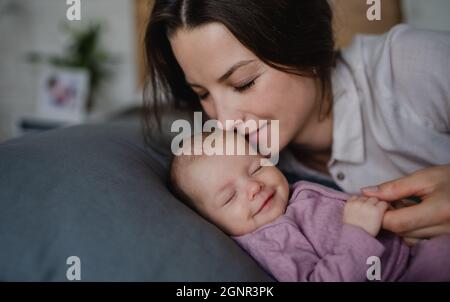 Felice giovane madre baciare la sua bambina neonato, sdraiata sul divano interno a casa. Foto Stock