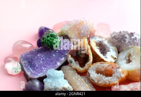 Gemme di vari colori. Geode ametista, quarzo rosa, agato, apatite, aventurina, olivina, turchese, acquamarina, cristallo di roccia giacciono su sfondo rosa Foto Stock