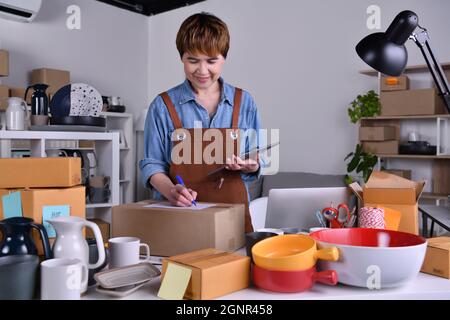 Donna asiatica matura imprenditore, imprenditore di affari che controlla l'indirizzo e il dettaglio di consegna prima della spedizione del prodotto. Online vendere lavoro di business a casa con Foto Stock