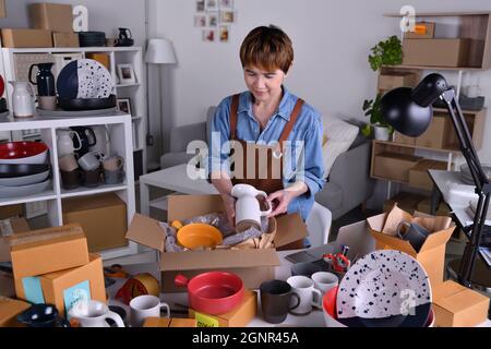 Donna asiatica matura imprenditore, imprenditore di affari che impacchettano i prodotti di ceramica in imballaggio per la consegna e la spedizione. Lavoro di vendita in linea di affari a hom Foto Stock