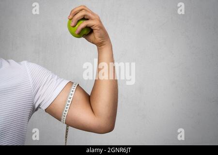 Giovane atletico che tiene una mela e mostra il suo bicipite. Sport e dieta per una vita sana. Foto di alta qualità Foto Stock