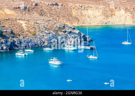 Lindos Beach vista panoramica baia con mare turchese chiaro barche turisti e sole su Rodi Grecia. Foto Stock