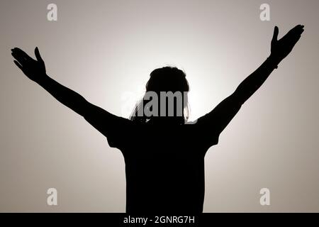 Silhouette al tramonto di donna fedele che prega. Concetto di religione, fede, preghiera e spiritualità. Foto Stock