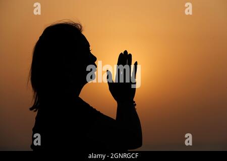 Silhouette al tramonto di donna fedele che prega. Concetto di religione, fede, preghiera e spiritualità. Foto Stock