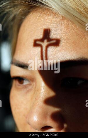 Ombra di un piccolo crocifisso sul volto di una donna cristiana. Fede e religione. Foto Stock