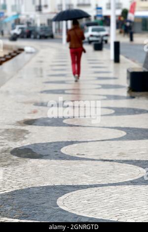 Vista posteriore di una donna con ombrello nero che cammina sulla strada. Nazare. Portogallo. Foto Stock