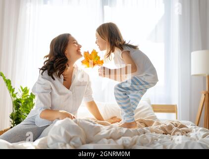 Una bella ragazza e sua madre godendo di sole mattina. Buon tempo a casa. Il bambino si sveglia dal sonno. Famiglia che gioca sul letto in camera da letto. Foto Stock
