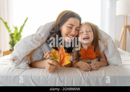 Una bella ragazza e sua madre godendo di sole mattina. Buon tempo a casa. Il bambino si sveglia dal sonno. Famiglia che gioca sul letto in camera da letto. Foto Stock