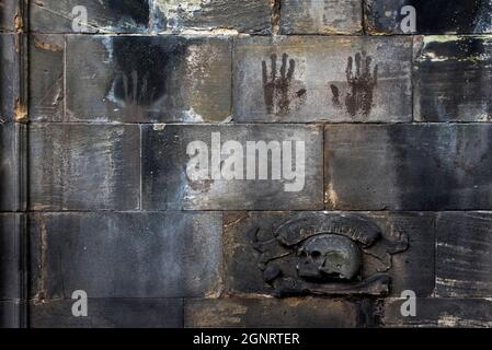 Stampe dall'aspetto spoky accanto a un teschio e a una croce ricordo mori su una parete a Greyfriars Kirkyard, nella città vecchia di Edimburgo. Foto Stock