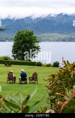 Washington, USA - 8 luglio 2021: Una coppia adulta si rilassa sulle sedie adirondack vicino al lago al Lago Quinault Lodge in una mattina nebbia Foto Stock