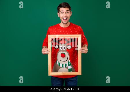 Foto ritratto uomo in maglia rossa sul natale sorridente mantenendo bordo di legno isolato colore verde sfondo Foto Stock