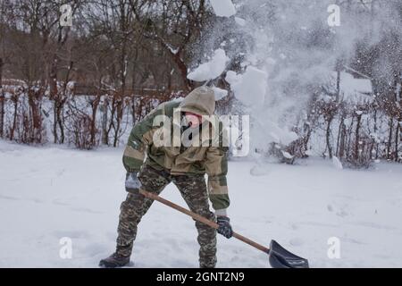 L'uomo libera il cortile della neve con Shovel. Nevicate pesanti in inverno. Alto livello di neve. Nevicate nevicate. Foto Stock