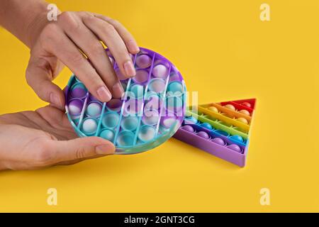 Donna hans utilizzando colore pastello rotondo popit giocattolo antistress per bambini e adulti su uno sfondo giallo. Il giocattolo antistress sensoriale flessibile lo schioccano intorno Foto Stock