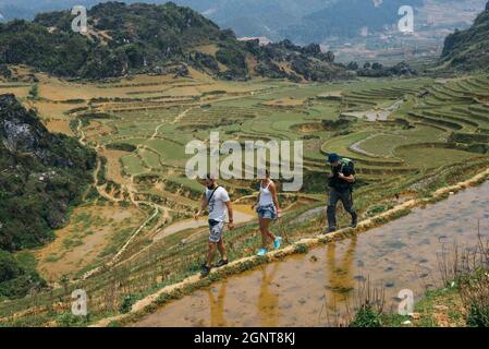 I turisti che si recano in montagna con zaino vicino a terrazze di riso a Sapa, Vietnam. Riflessione delle persone nelle risaie durante il tour a piedi. Foto Stock