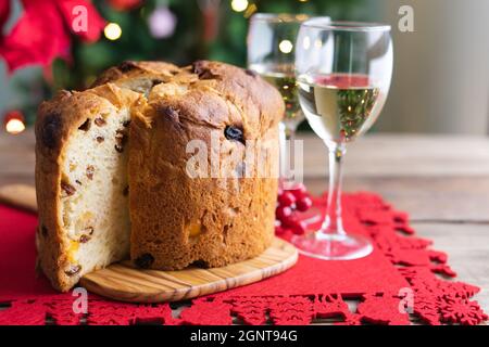Bicchieri di panettone e vino bianco su un tavolo di legno con decorazioni natalizie e albero sullo sfondo. Spazio di copia. Foto Stock