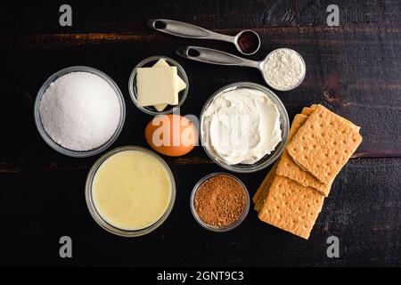 Mini Eggnog Cheesecake ingredienti: Eggnog, formaggio spalmabile e altri ingredienti per cupcake eggnog su sfondo di legno Foto Stock