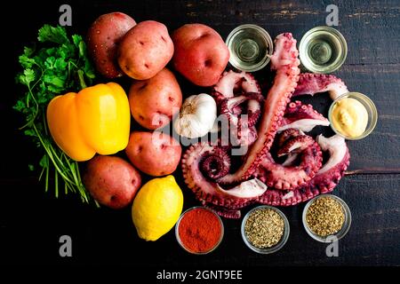 Polpo di stile spagnolo con patate ingredienti: Tentacoli di polpo crudo, verdure, erbe e altri ingredienti su sfondo di legno Foto Stock