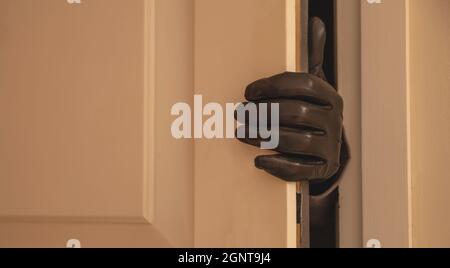 Housebreaking, burglary concetto. Mano guantata che apre la porta d'ingresso, burglar che entra illegalmente la casa Foto Stock