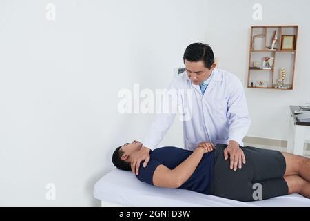 Shot orizzontale di fisioterapista asiatico maturo che lavora con il giovane paziente maschio recuperare la sua flessibilità backbone Foto Stock