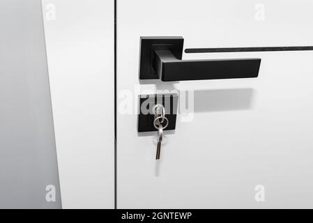Moderna porta bianca con maniglia nera opaca e serrature magnetiche, serratura con chiave inserita. Foto Stock