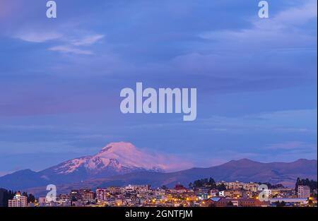 Città di Quito al tramonto durante l'ora blu con il vulcano Cayambe, Ecuador. Foto Stock