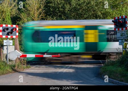 un treno che passa su un incrocio a livello nel sussex ovest. a livello ferroviario che attraversa una strada con luci rosse lampeggianti per l'attraversamento della sicurezza in sussex. Foto Stock