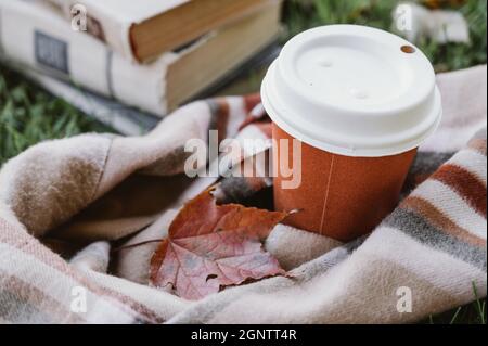 Composizione autunnale. Tazza di cartone arancione di caffè. Foglia di acero su sciarpa marrone caldo. Pila di libri. Foto Stock