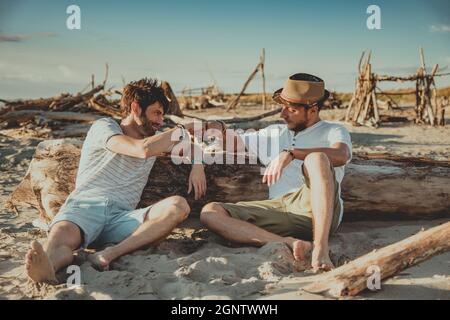 Due ragazzi seduti sulla spiaggia si salutano con i loro pugni. Giovani che suonano i loro pugni per salutarsi a vicenda Foto Stock